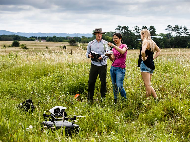 Dr. Paul Lorah works with Alice Ready and Emma Rinn in a field. 