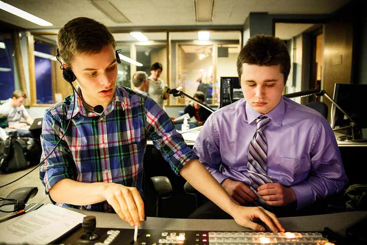 Two students operate a camera switching board in a media studio.