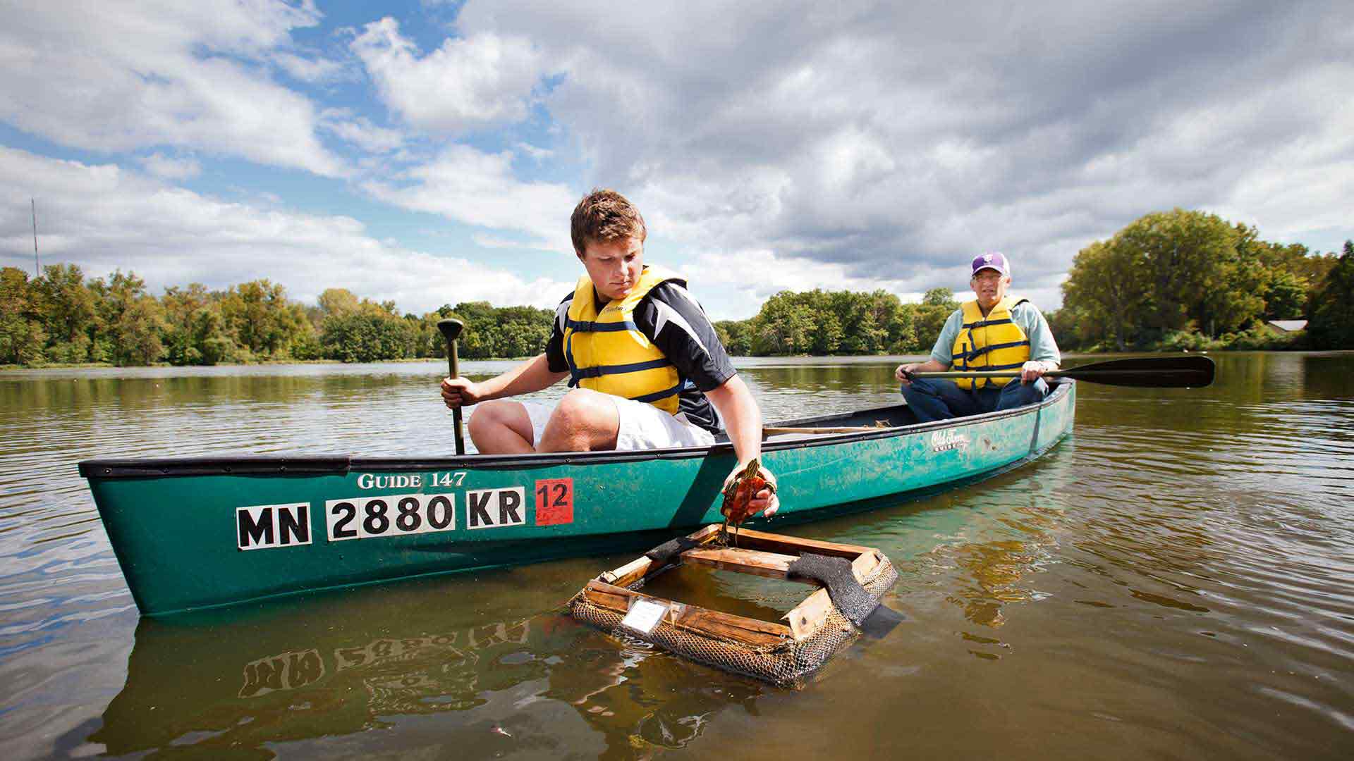 A student and faculty member examine a turtle from a canoe in a river. 