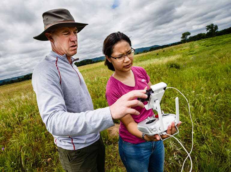 Dr. Paul Lorah and alumna Emma Rinn examine a drone in the middle of a field. 