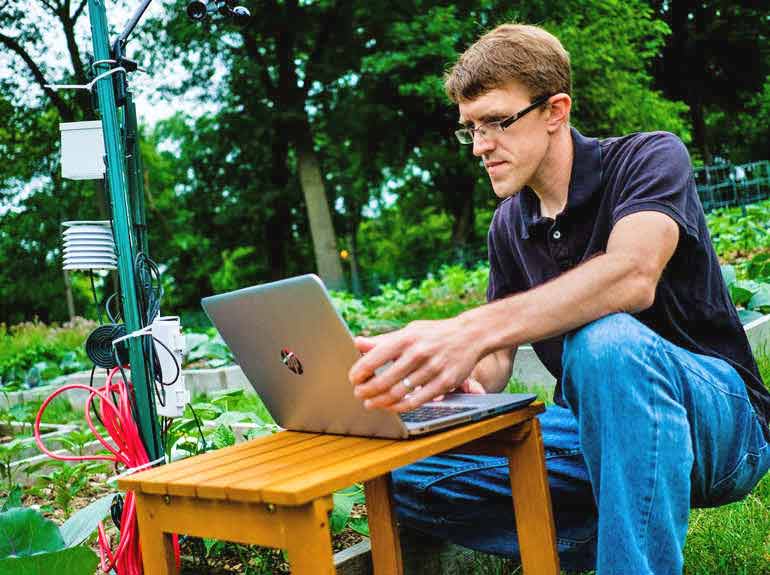 Photo of Dr. Gaston “Chip” Small looking at a computer in the middle of field of an experimental garden. 