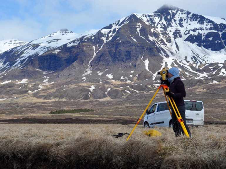 A student examines a landscape in Iceland with a mountain in the background. 