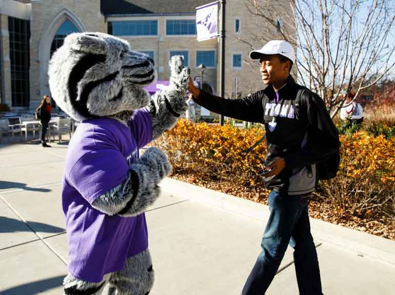 The St. Thomas mascot, Tommie, high-fives a student as they walk into the Anderson Student Center.