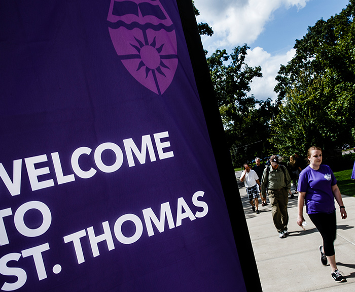 Student on campus walking by welcome to St. Thomas sign.
