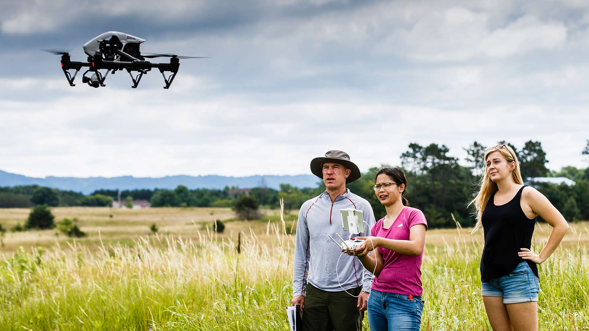 Professor and two students conduct research with the help of a drone in a field.