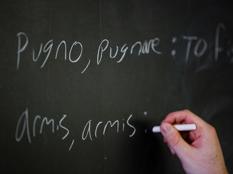 Student writing in Latin on a chalkboard.