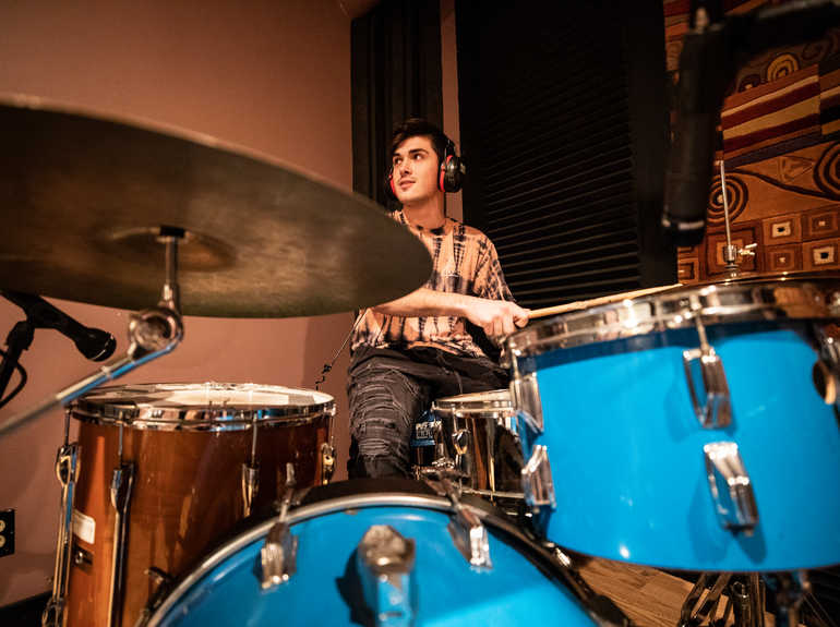 A student plays drums in a recording studio.