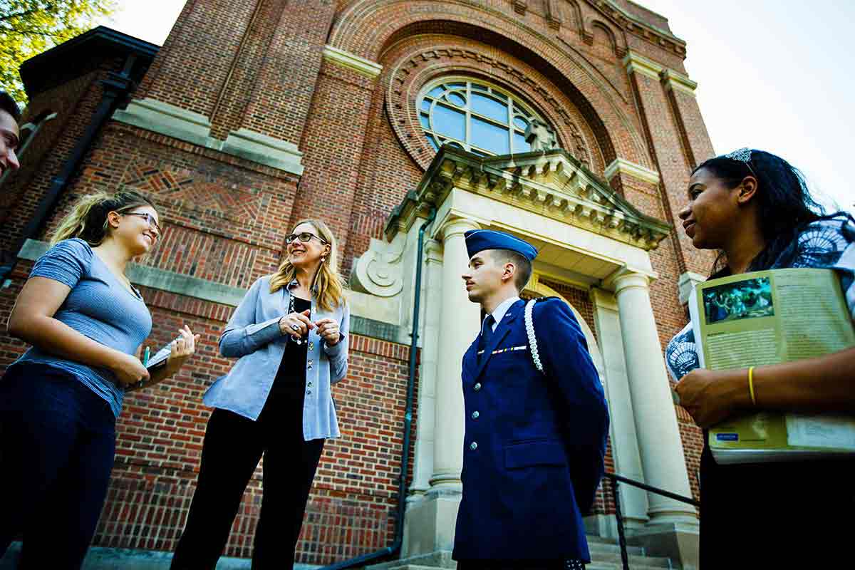 A Saint Thomas professor talks to a cadet and two other students in front of the Chapel of Saint Thomas Aquinas.