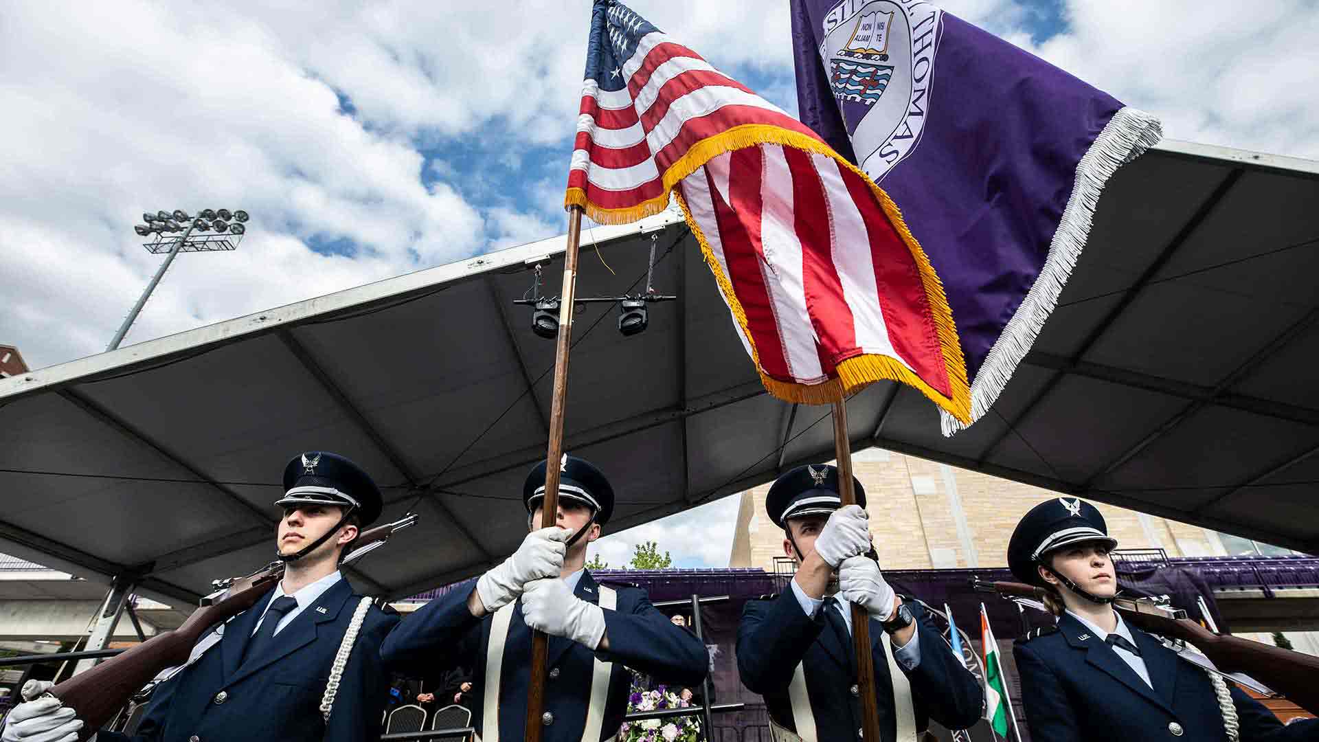 Four cadets stand at attention while performing a military honor guard ceremony during a Saint Thomas commencement ceremony.
