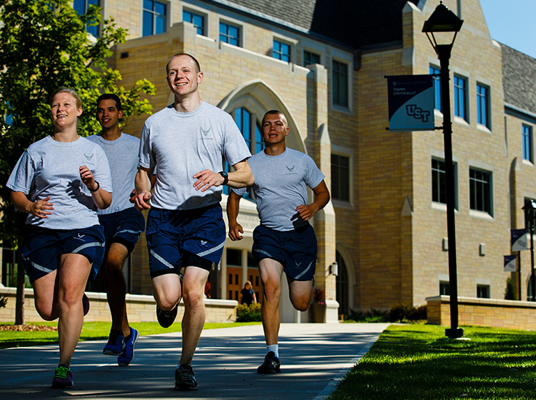 Four cadets run in physical fitness attire across Saint Thomas campus.
