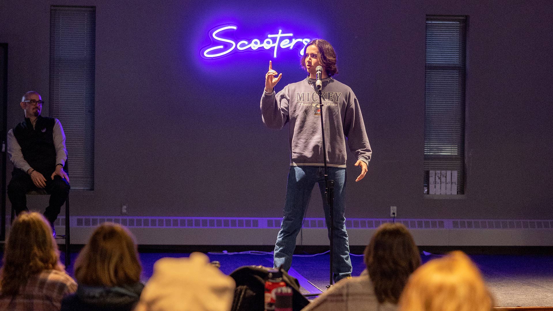 A student gestures and speaks on stage during a storytelling event at Scooter's on the St. Thomas campus