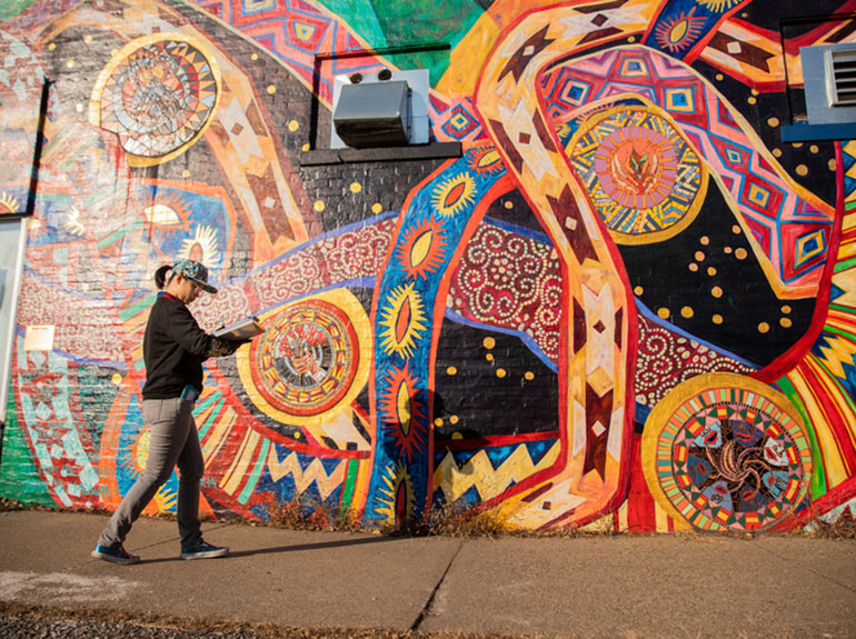A student writes notes as she walks by a mural.