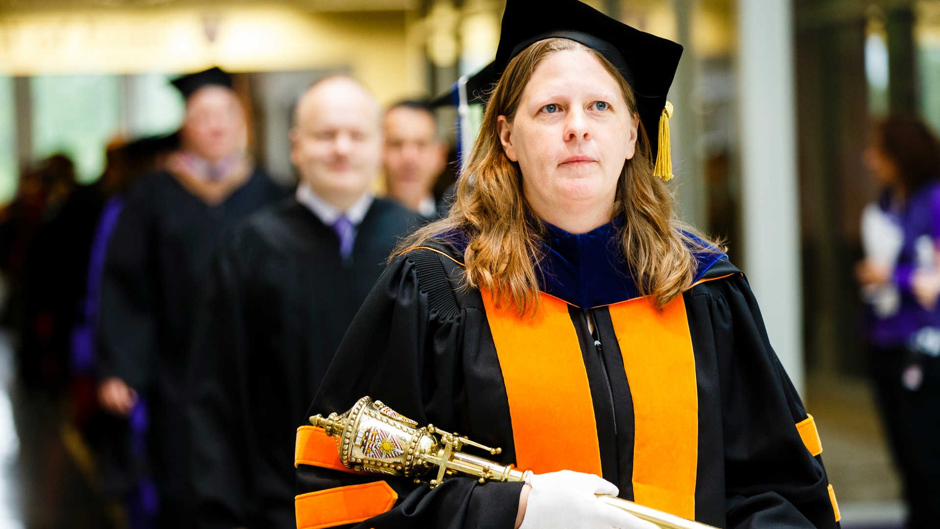Professor Kris Wammer carries the mace during commencement