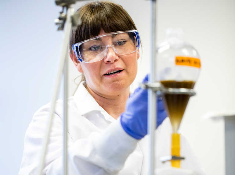 Dr. Jeni McDermott examines lab equipment with rock sediment in it. 