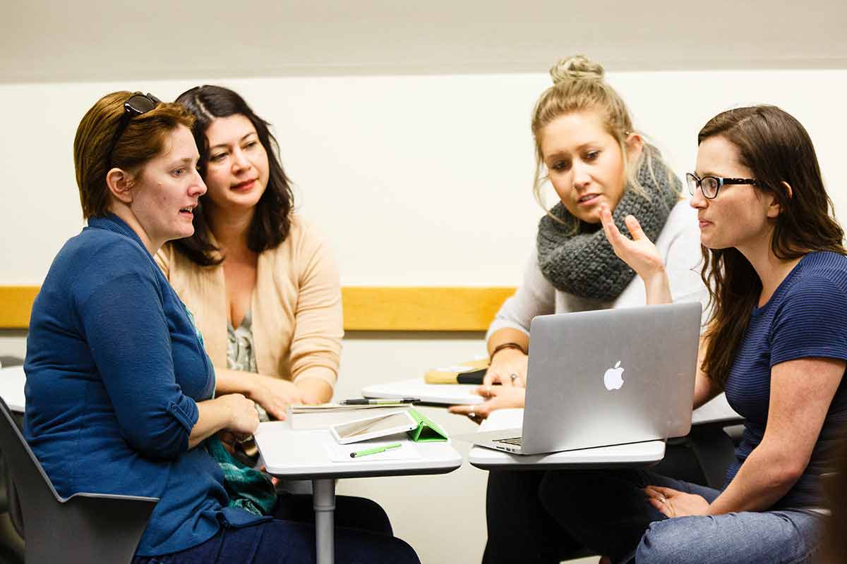 Three graduate students, along with professor, work in a group during class.