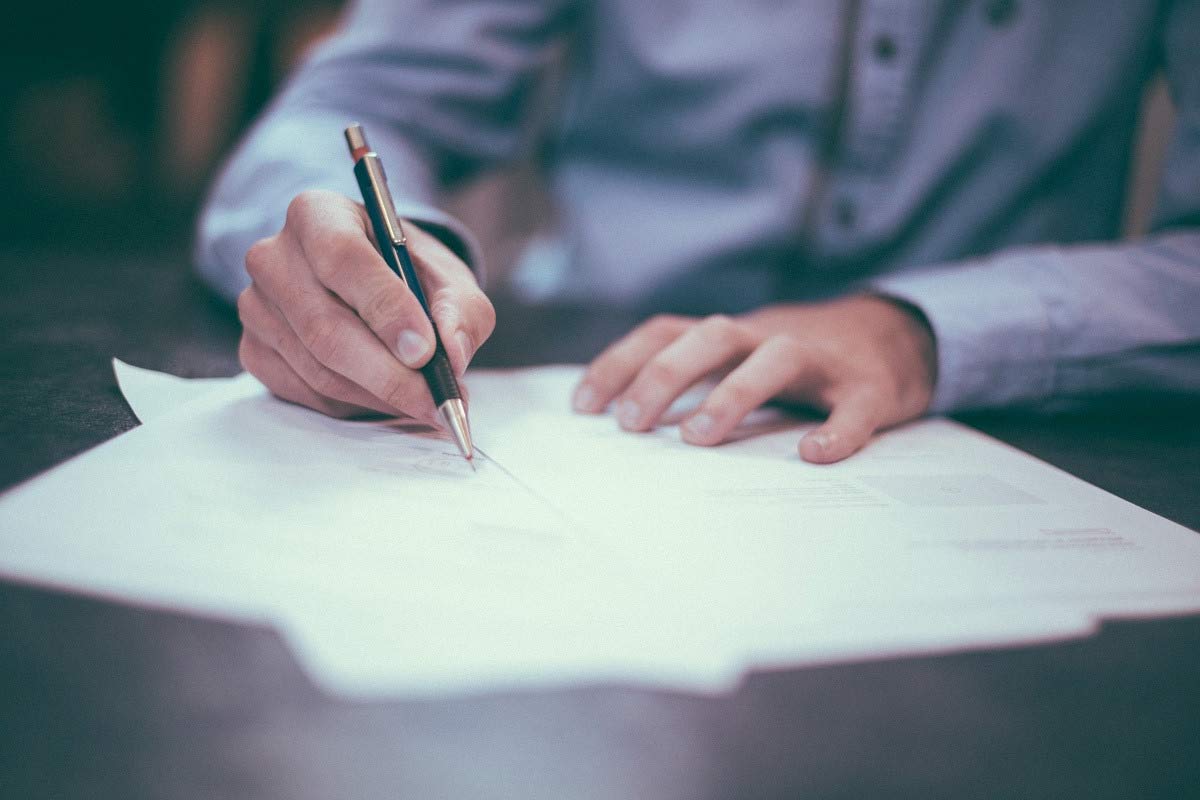Stock photo of a person writing on a piece of paper on a wooden desk.
