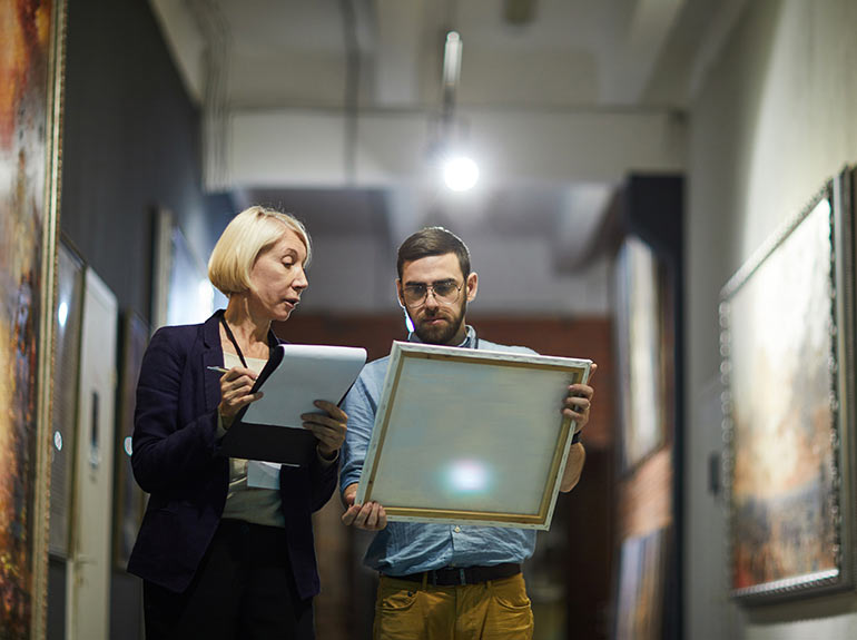 Two people walking while examining a painting.