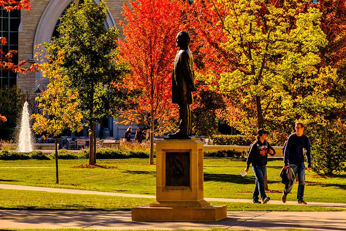Students walking past the statue of John Ireland on campus in the fall.