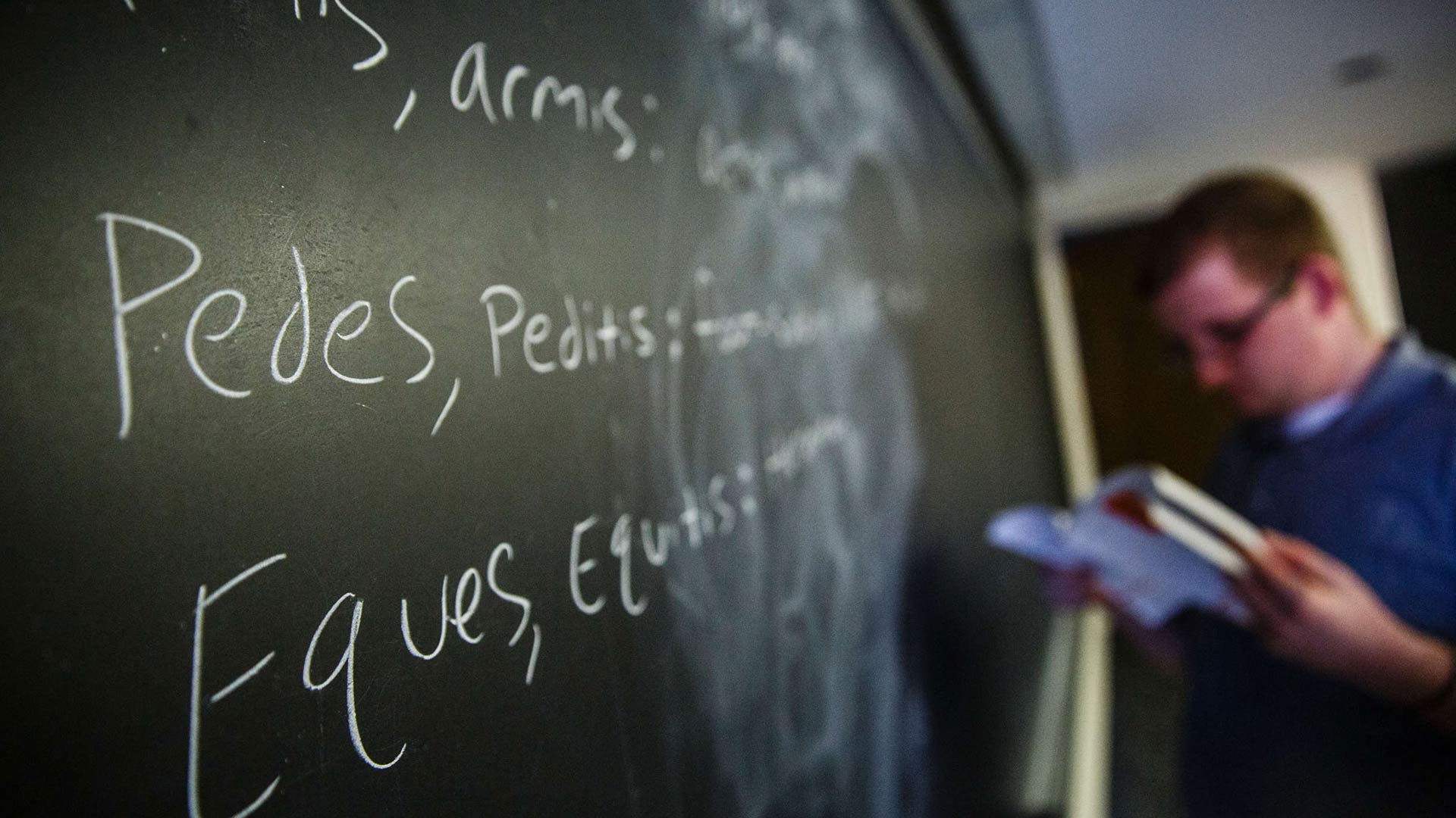 A student writes Latin words on a blackboard during a Latin class. 