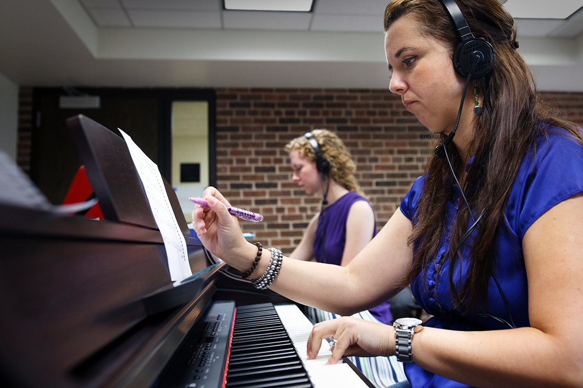 Student with headphones sitting at a piano marking a notation.