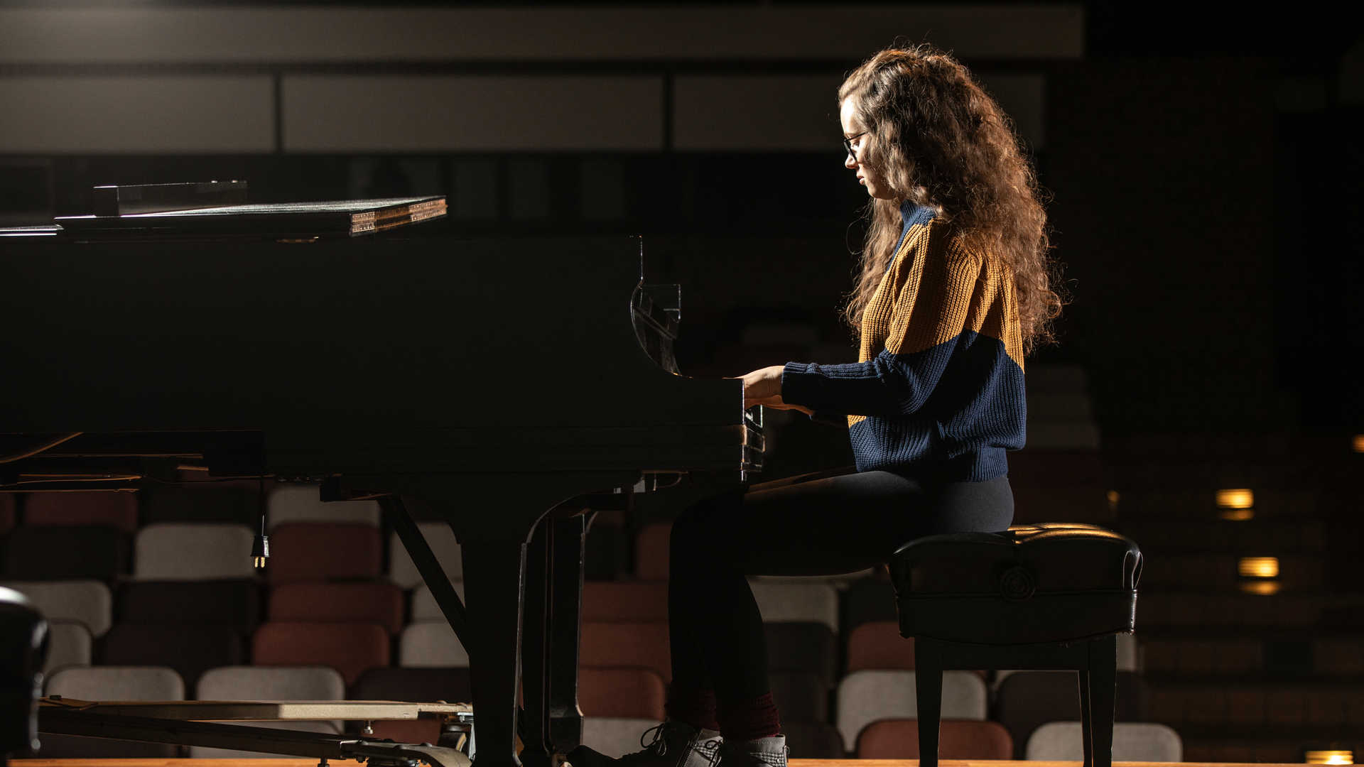 A student plays the piano in a music hall.