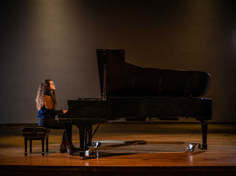 A student plays the piano on a stage.