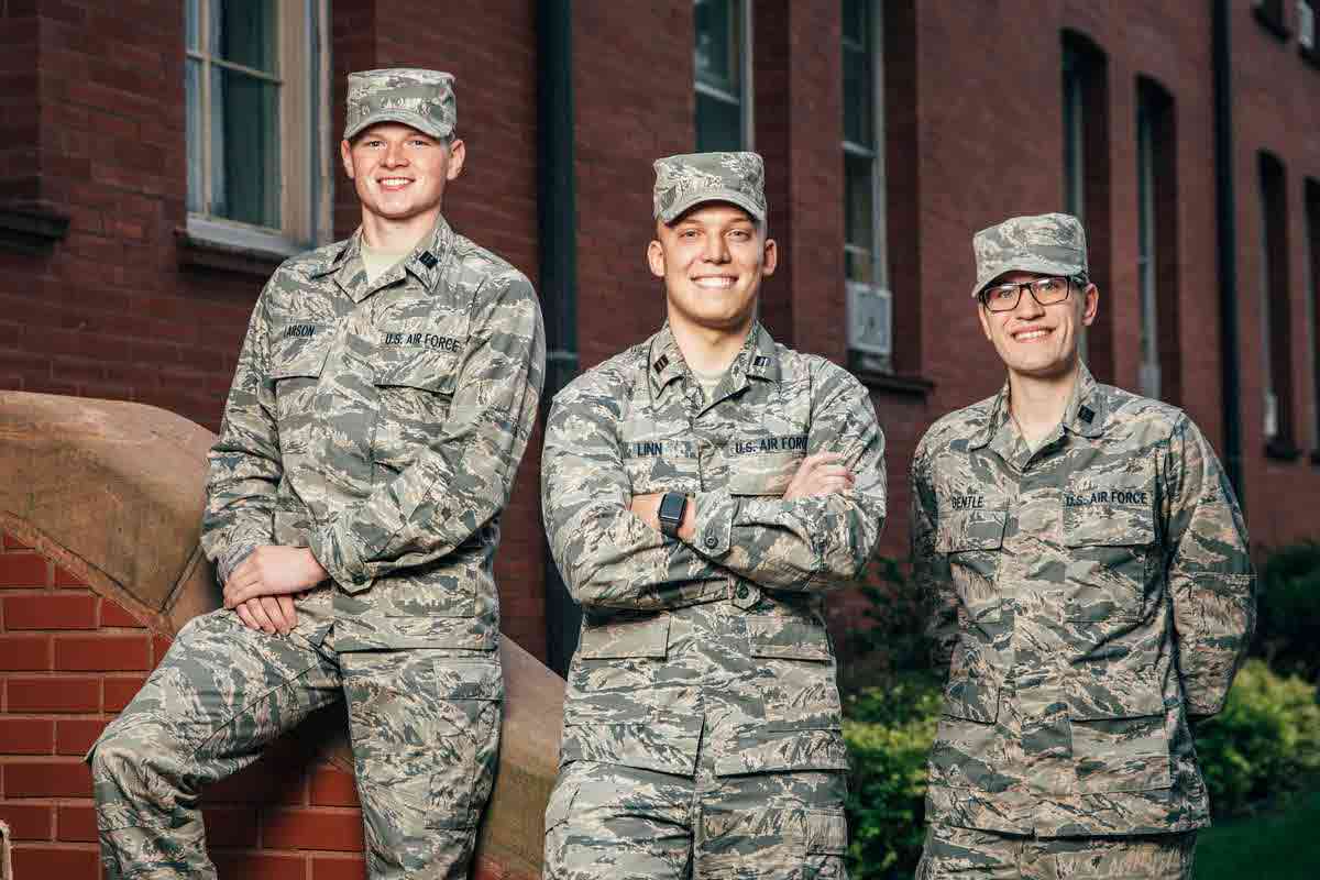 Three Air Force ROTC cadets pose for a photo in front of a brick building. 