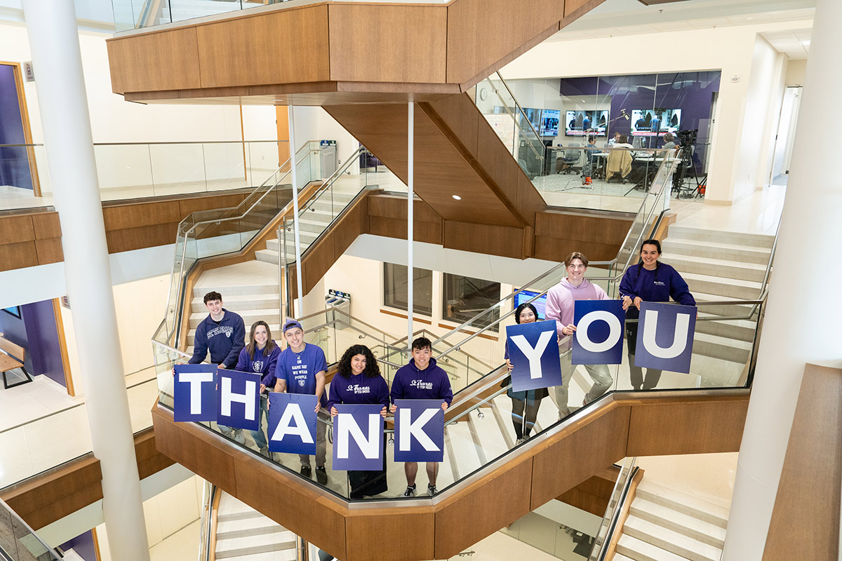 Students hold "thank you" signs on the staircase of Schoenecker Center