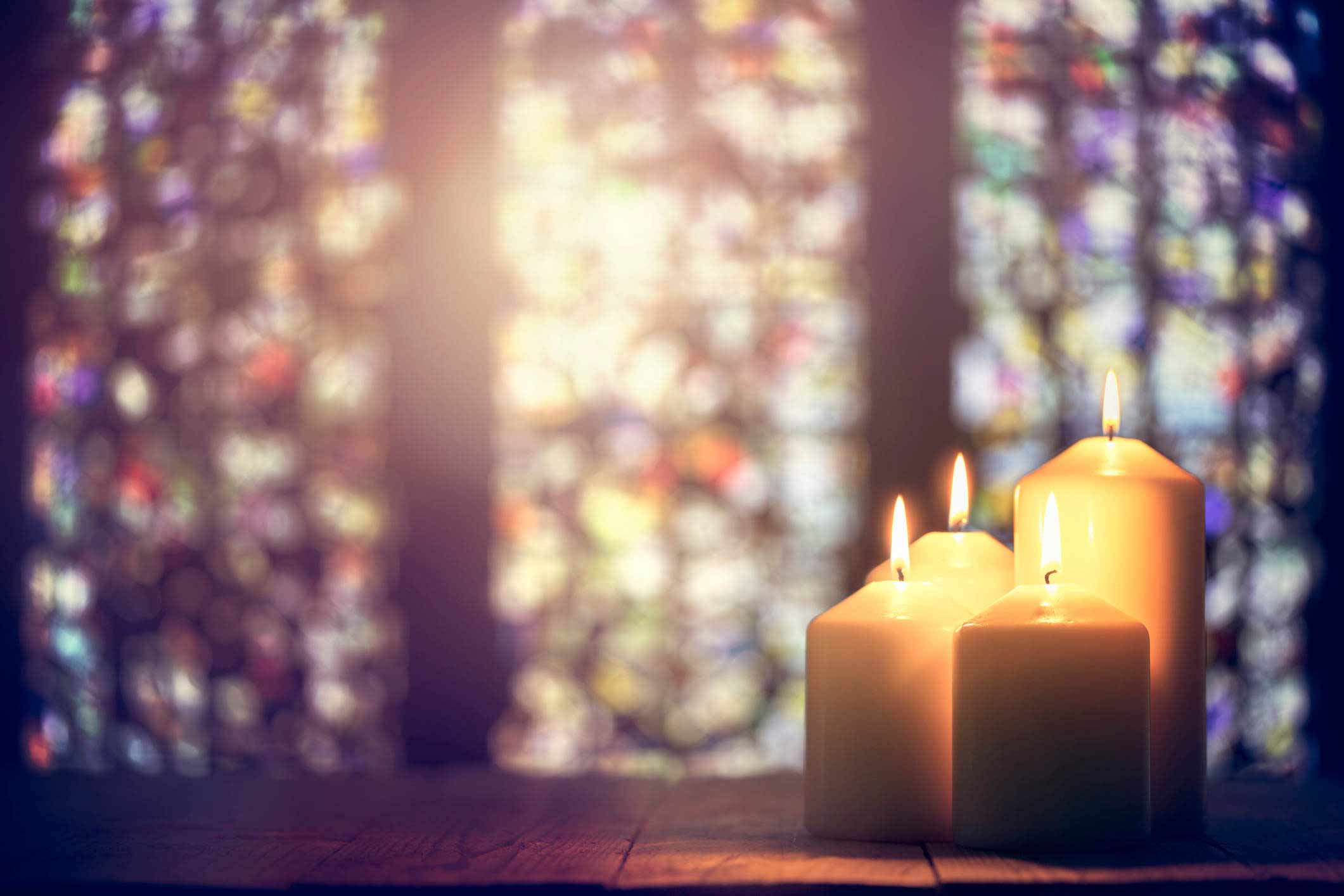 Lit candles in front of a stained glass window.